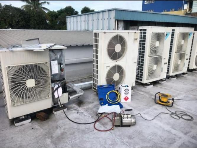 A rooftop bank of condenser units with vacuum pump and gauge set during a commercial install